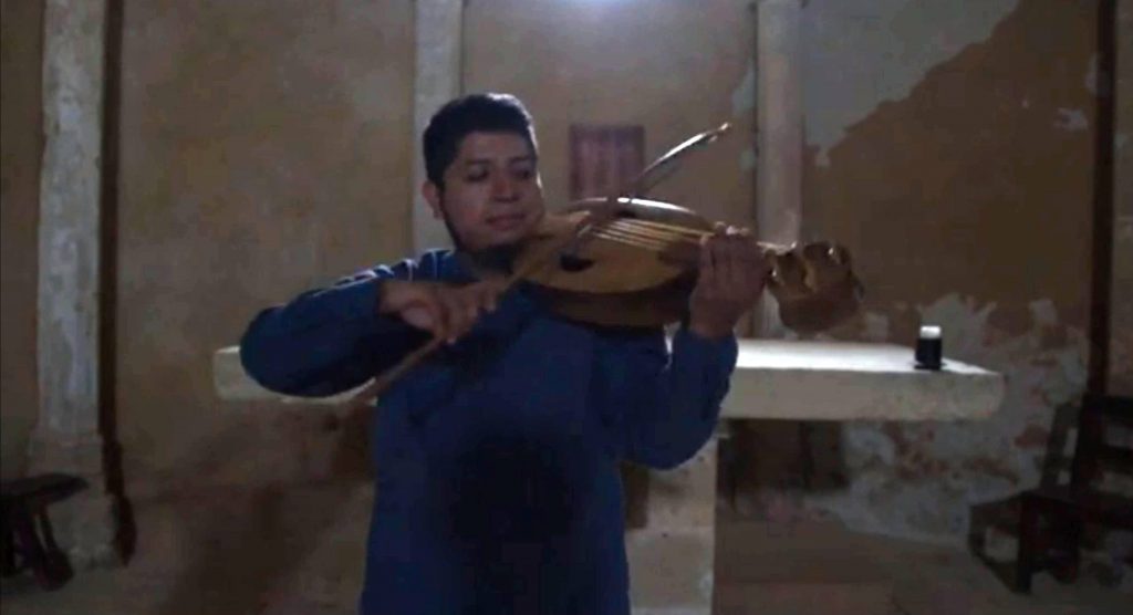 Gabriel Alejandro Hernández plays a 5 string fiddle. (Click on picture, opens in new window.) He has some curvature on the bridge, so his drone playing is on adjacent strings only, rather than the whole string block, and he demonstrates the plucked bourdon: Aurea personet lira, attributed to Fulbert de Chartres, France, 952/970–1028.